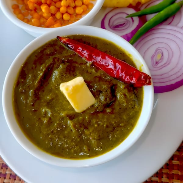 A bowl of Saffron Indian Cuisine's green saag with butter, red chili, and sliced onions.