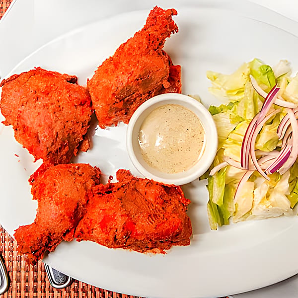 Three pieces of Saffron Indian Cuisine's Tandoori Chicken, with a side of salad and dipping sauce.
