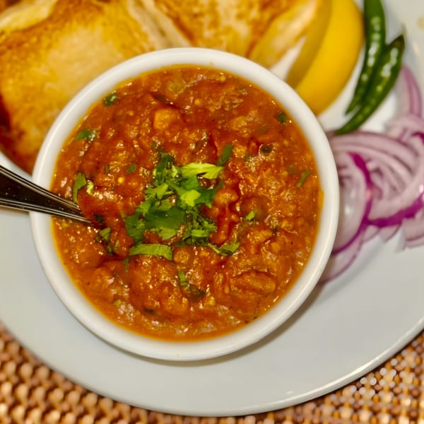 A bowl of Indian pav bhaji, garnished with cilantro, served with bread, lemon, and onions.
