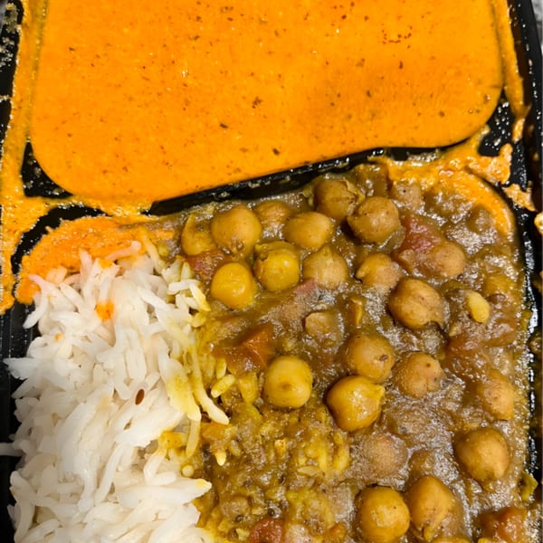 Indian chickpea curry with white rice and a side of orange sauce in a black container.